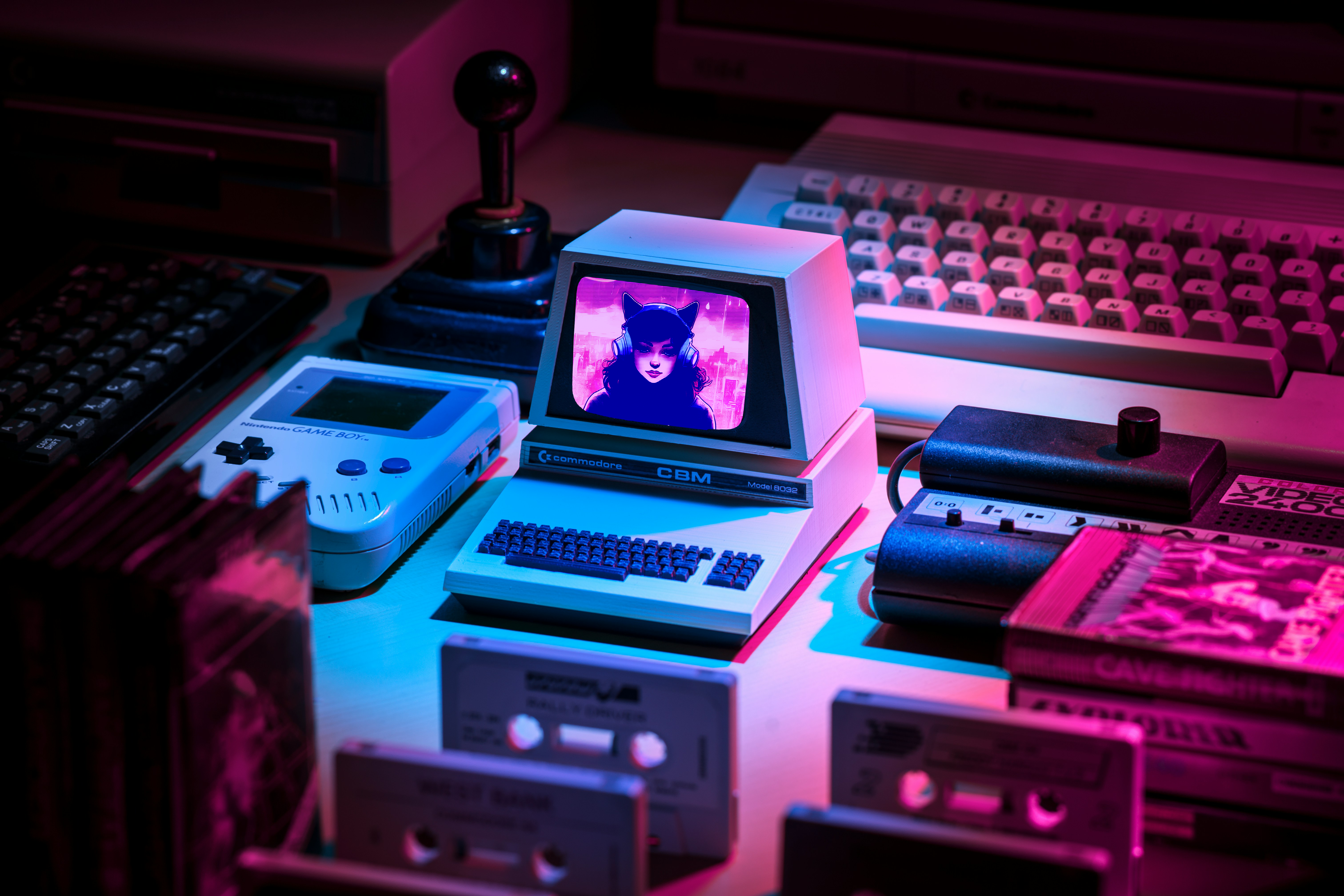 Retro scene featuring vintage computers, a Game Boy, cassette tapes, and a small monitor displaying a witchy girl with cat ears and headphones, bathed in neon pink and blue lighting.